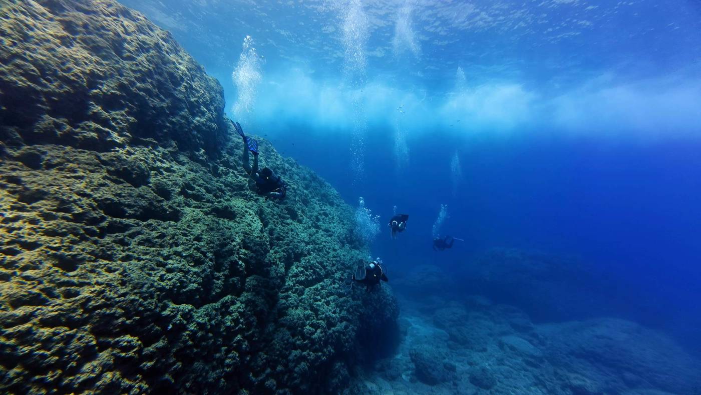 Skupina potápěčů ve velmi čisté vodě, na nimi právě projel motorový člun